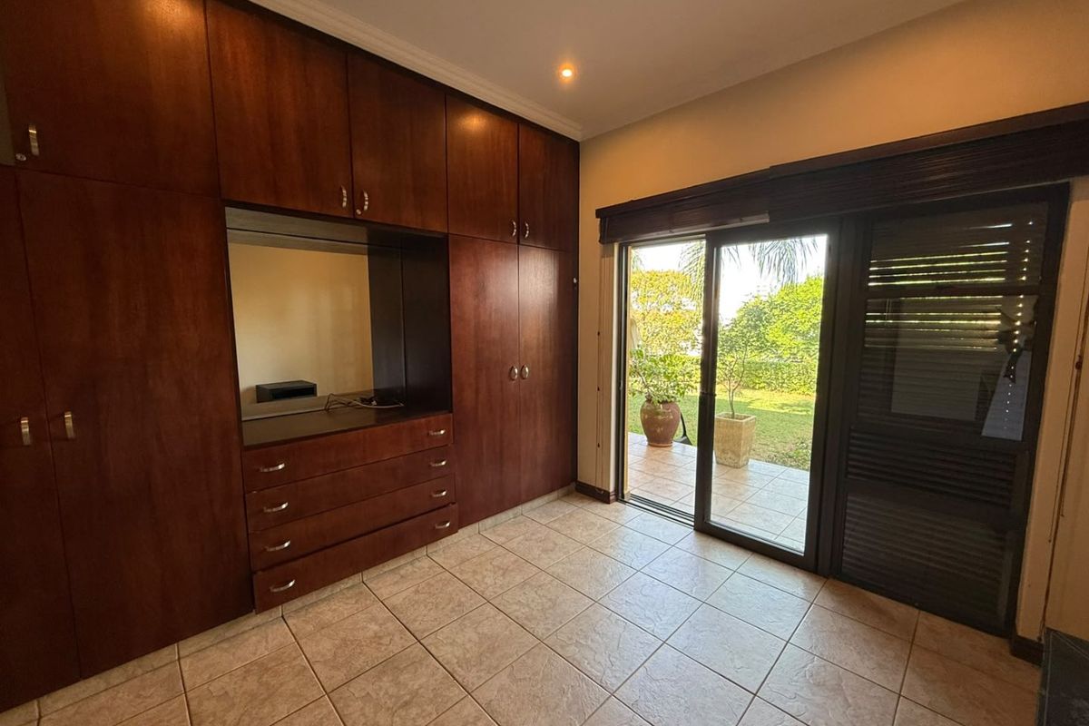 Spacious bedroom featuring extensive dark wood built-in cabinetry, tiled flooring, and large sliding glass doors providing direct access to the garden area.