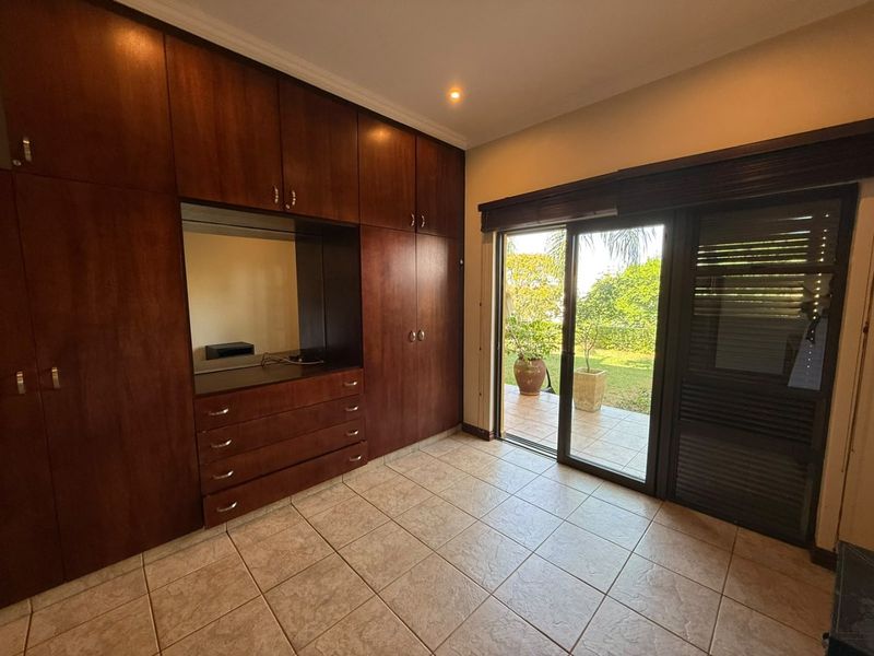 Spacious bedroom featuring extensive dark wood built-in cabinetry, tiled flooring, and large sliding glass doors providing direct access to the garden area.