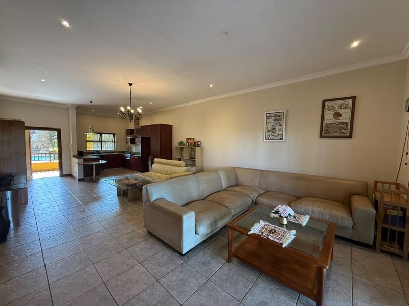 Spacious open-plan living area featuring tiled floors, recessed lighting, and a functional kitchen with built-in cabinetry and appliances, leading to an outdoor patio.