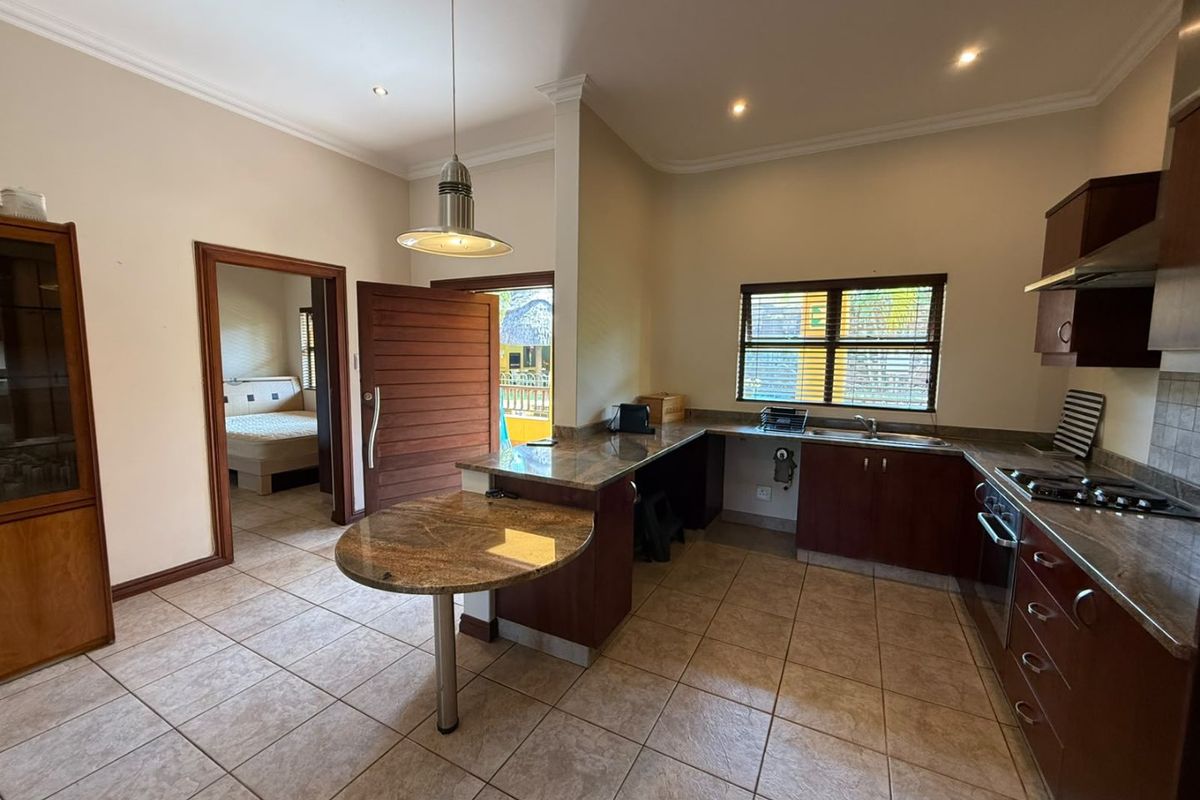 A functional kitchen featuring granite countertops, dark wood cabinetry, built-in gas hob, and tiled flooring, with direct access to an adjacent bedroom.
