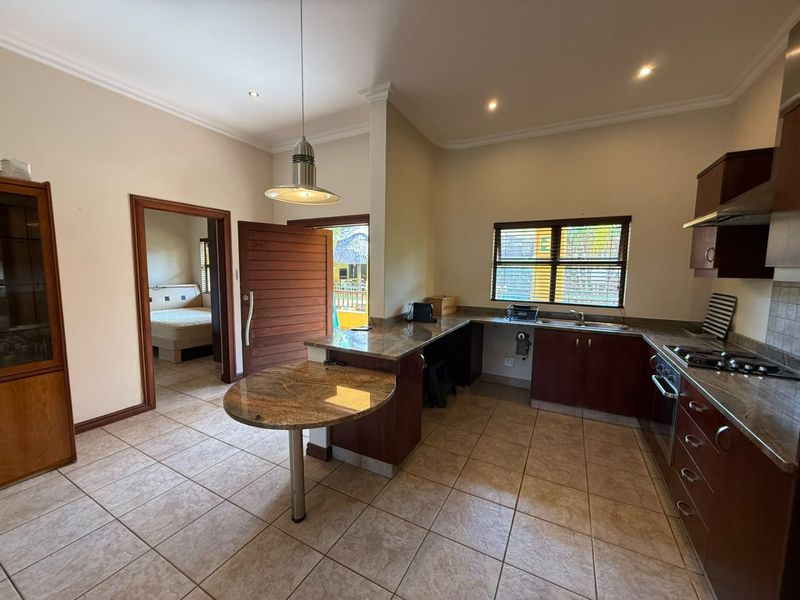 A functional kitchen featuring granite countertops, dark wood cabinetry, built-in gas hob, and tiled flooring, with direct access to an adjacent bedroom.