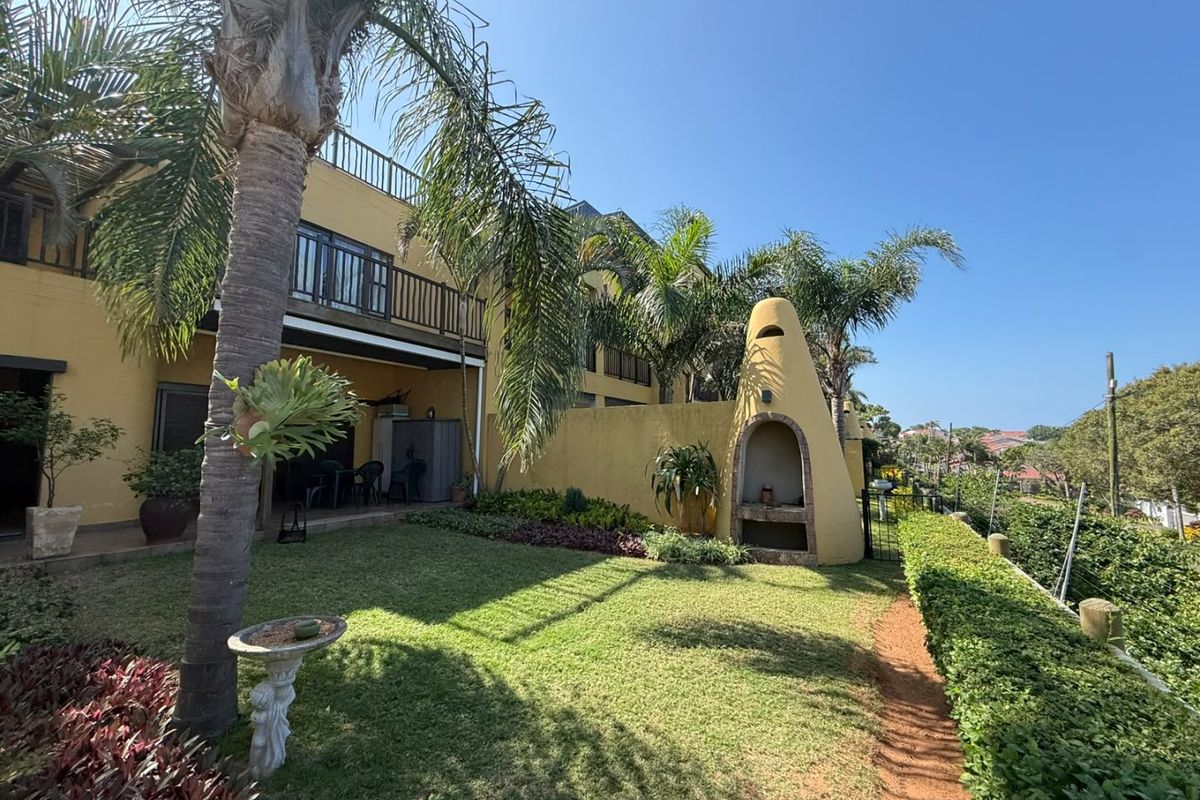 Rear exterior view of the apartment featuring a private garden, built-in braai, and an upper-level balcony.