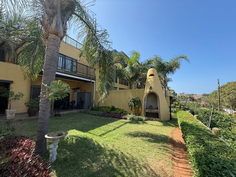 Rear exterior view of the apartment featuring a private garden, built-in braai, and an upper-level balcony.