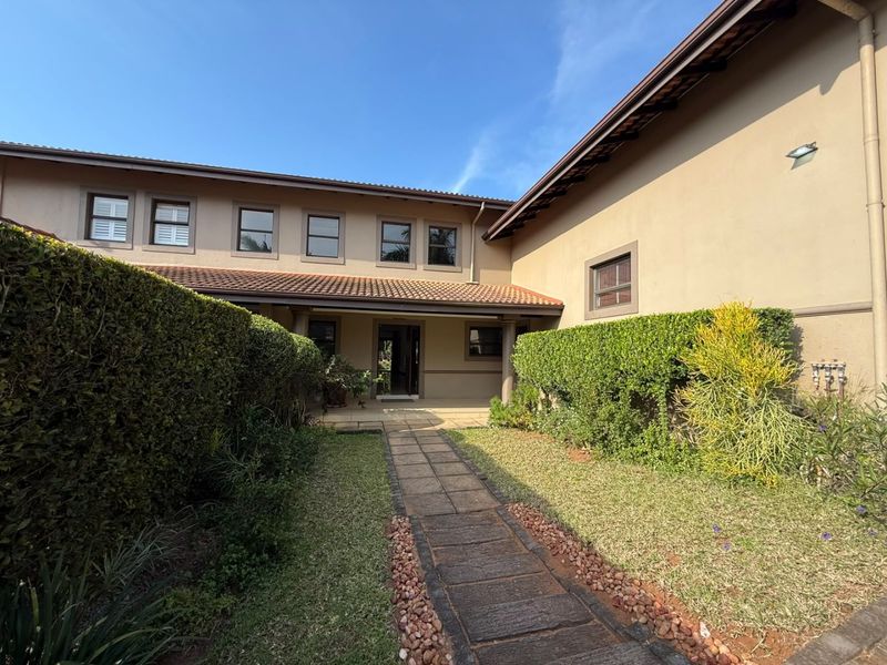A well-maintained townhouse entrance featuring a paved walkway leading to the front door, framed by manicured hedges and a neat garden.