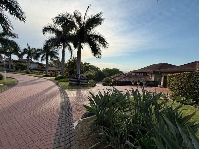 A view of the paved driveway and entrance area of the Cocohaven townhouse complex, featuring well-maintained landscaping and tiled roof architecture.
