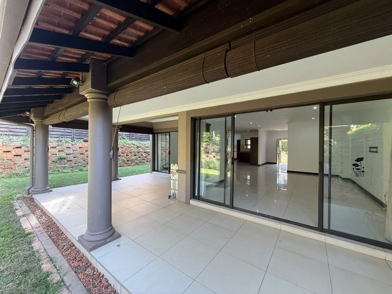 Spacious covered patio featuring tiled flooring and sliding glass doors, providing seamless indoor-outdoor flow to the garden area.