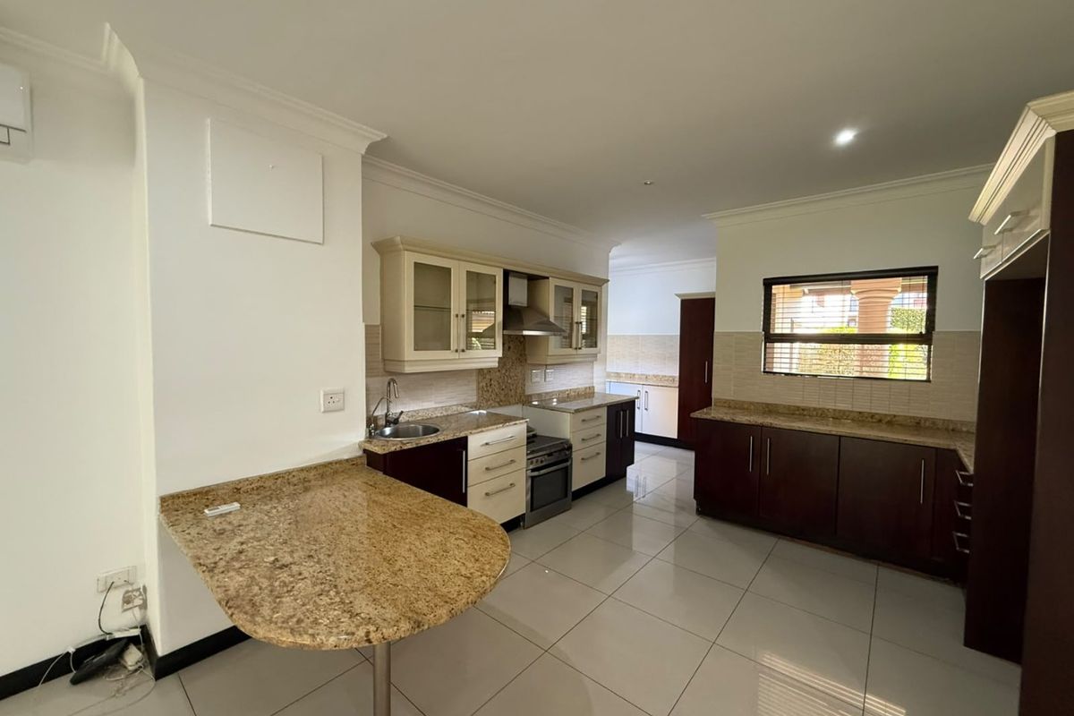 Spacious kitchen featuring granite countertops, ample built-in cabinetry, a stainless steel extractor fan, and tiled flooring in a clean, well-maintained townhouse setting.