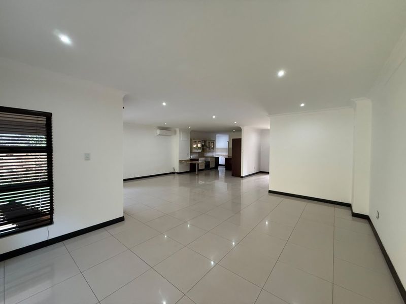 Spacious open-plan living area featuring neutral tiled flooring, recessed downlighting, and an integrated kitchen space, offering a bright and versatile layout.