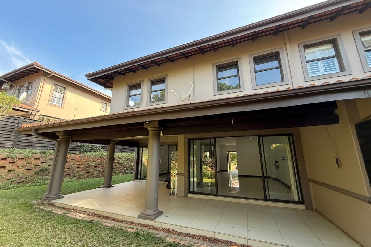 Spacious covered rear patio with tiled flooring, overlooking a landscaped garden and retaining wall, featuring large sliding glass doors leading into the home.