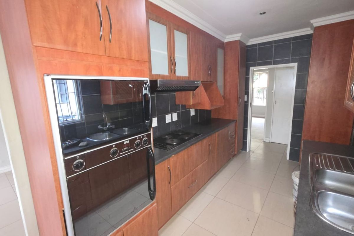 A functional kitchen featuring wood-finish cabinetry, built-in oven, electric hob, extractor fan, and double stainless steel sink with tiled splashbacks and flooring.