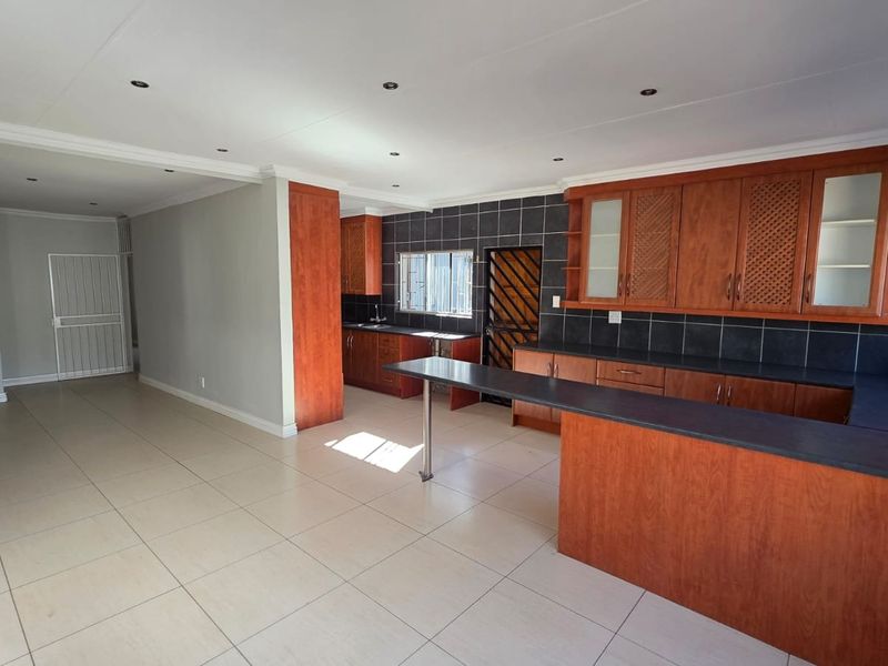 Spacious open-plan kitchen and living area featuring extensive wooden cabinetry, a breakfast bar, tiled flooring, and recessed lighting.