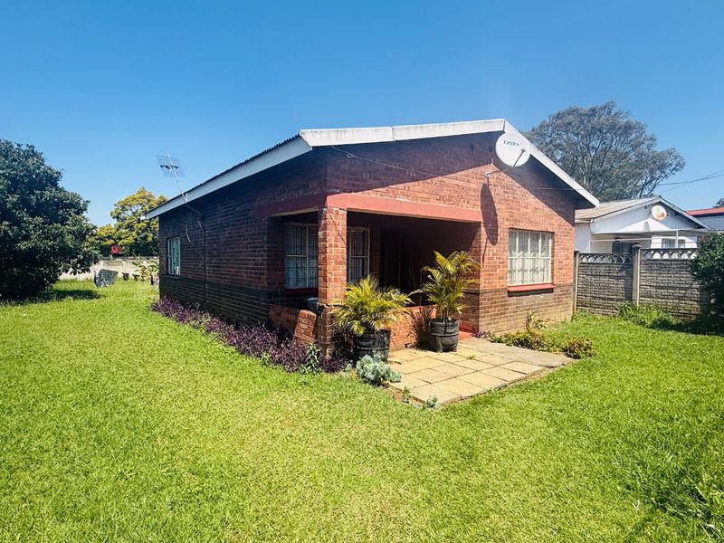A single-story brick townhouse featuring a covered front porch, metal roofing, and a surrounding lawn area.
