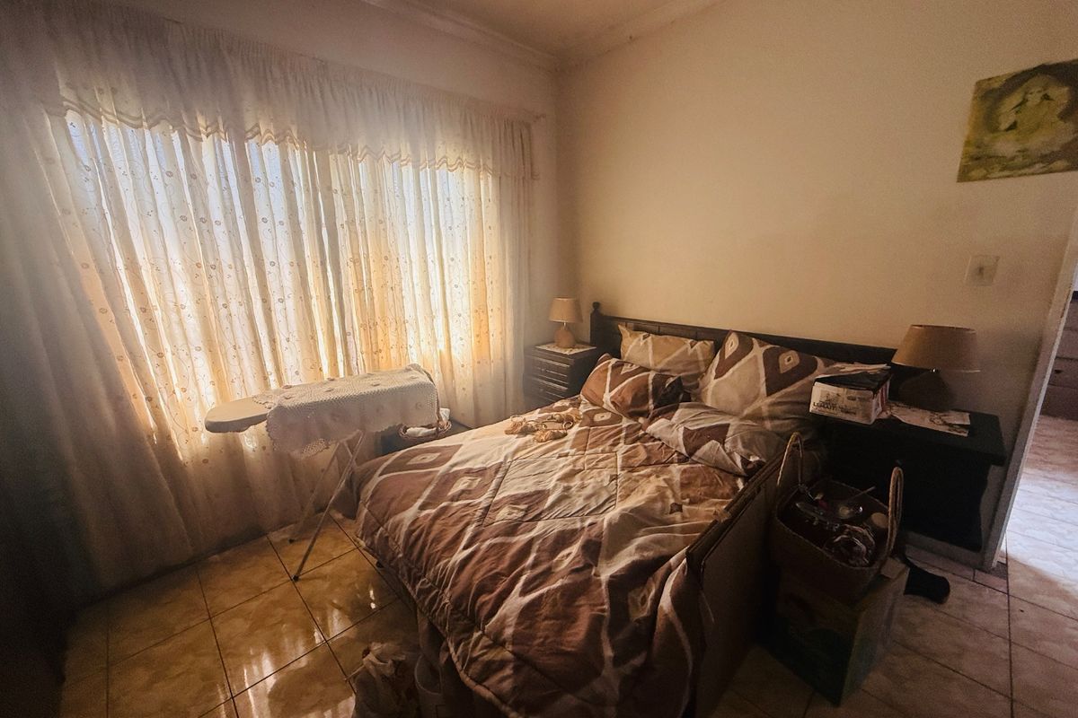 A bedroom featuring tiled flooring and large windows with curtains, offering a functional space that could benefit from modern updates.