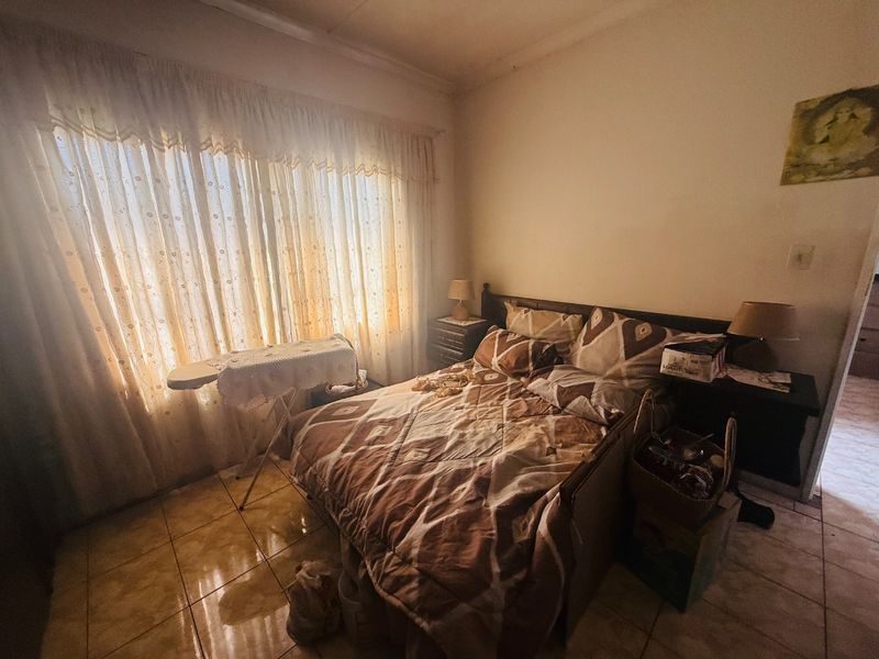 A bedroom featuring tiled flooring and large windows with curtains, offering a functional space that could benefit from modern updates.