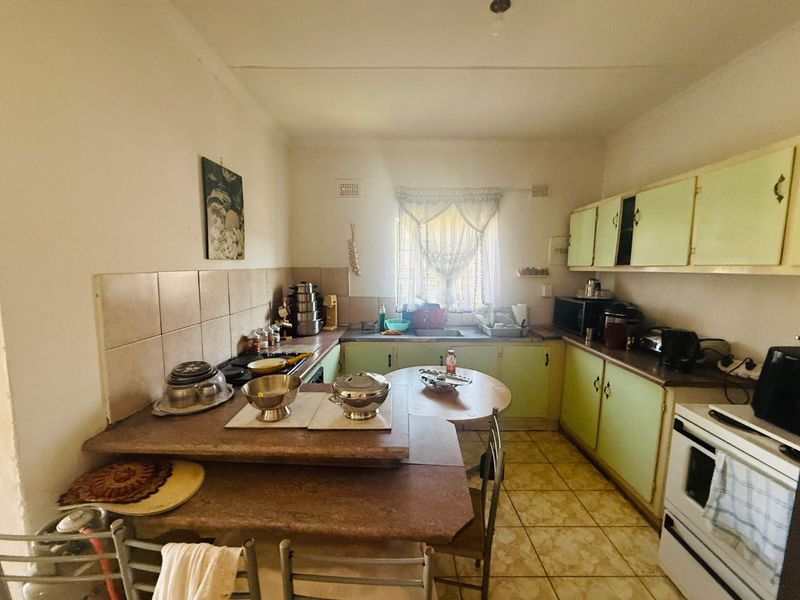 A functional kitchen featuring original cabinetry, laminate countertops, tiled backsplash, and ceramic flooring, offering potential for a modern renovation.