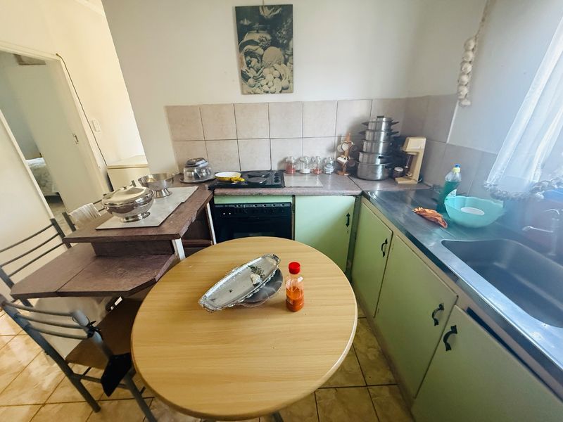 A functional kitchen featuring built-in oven, hob, stainless steel sink, and tiled backsplash with dated cabinetry and flooring.