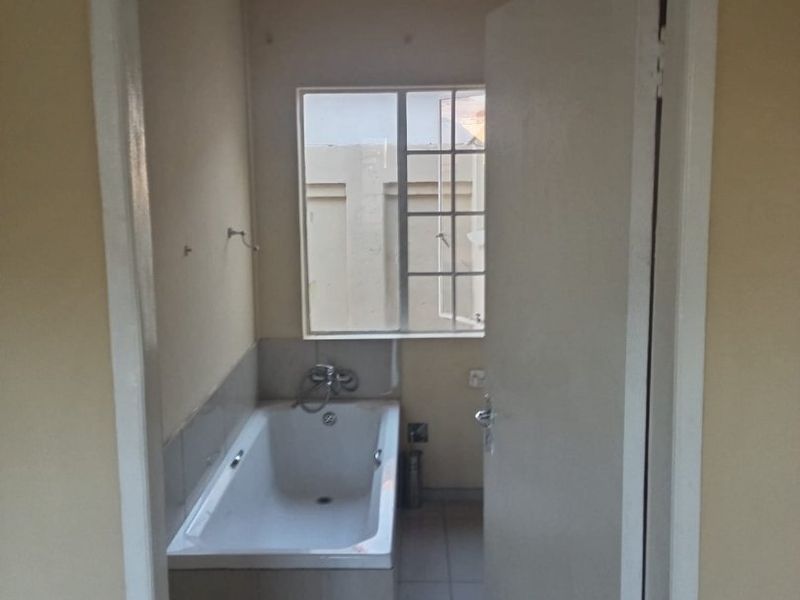 A functional bathroom featuring a built-in bathtub, tiled flooring, and a window with security bars, offering a clean and simple layout.