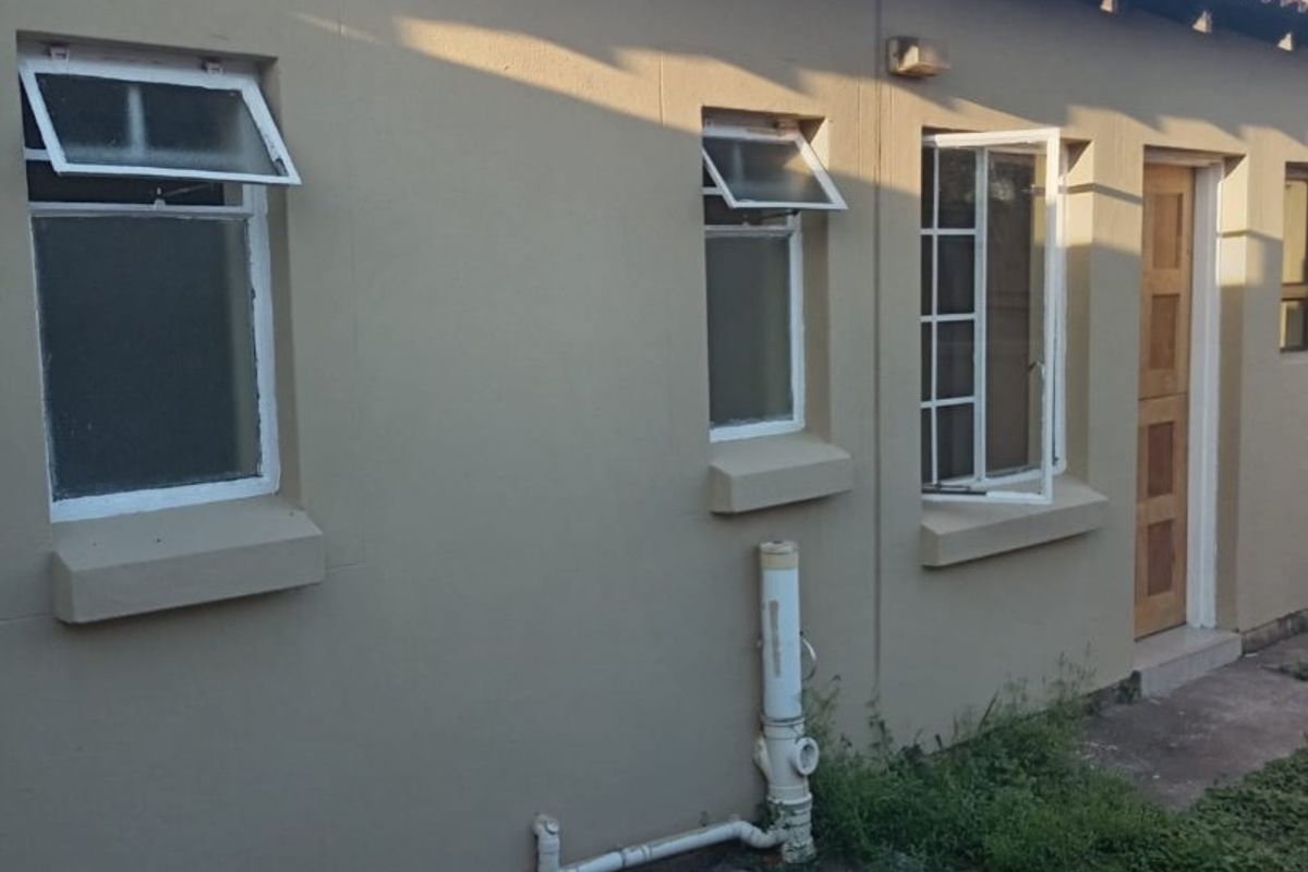 Rear exterior view of the house featuring tiled roofing, casement windows, and exposed external plumbing along the concrete pathway.