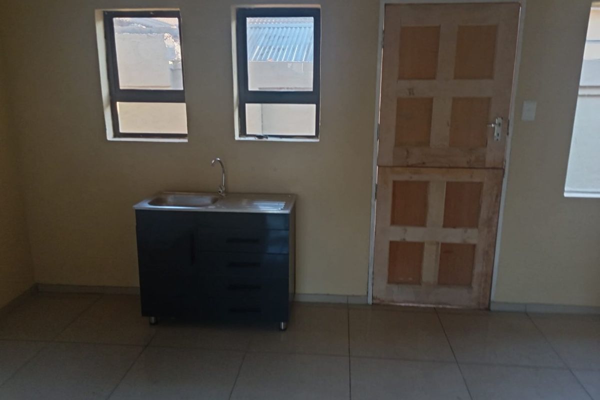 A basic kitchen area featuring a single sink unit, tiled flooring, and a wooden stable door, presenting a blank canvas for potential renovation.
