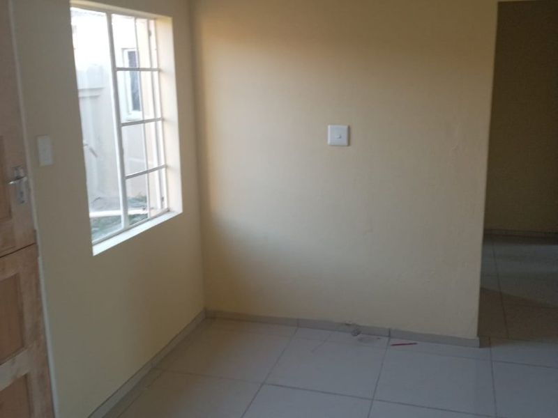An empty living area featuring neutral wall paint, tiled flooring, and a window with security bars.