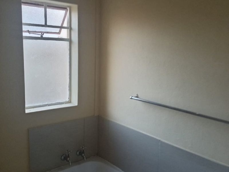 A functional bathroom featuring a built-in bathtub with tiled splashback, a metal towel rail, and a casement window.