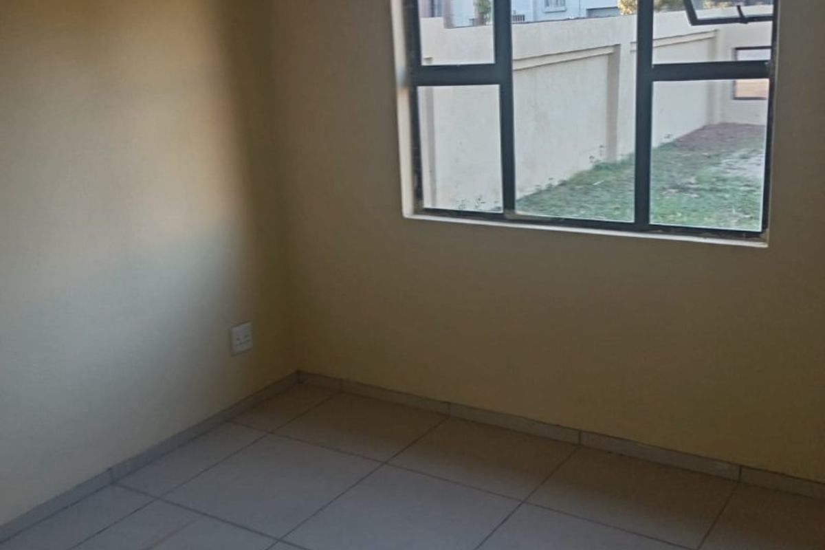 A vacant bedroom featuring neutral wall paint, tiled flooring, and an aluminium-framed window overlooking the exterior property boundary.