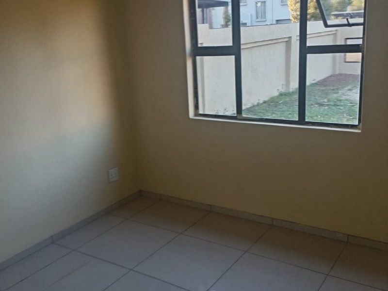 A vacant bedroom featuring neutral wall paint, tiled flooring, and an aluminium-framed window overlooking the exterior property boundary.