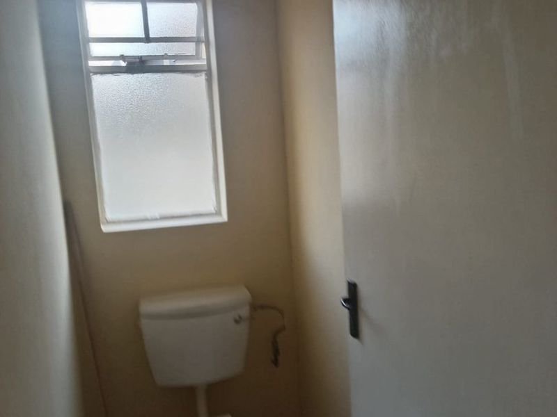 A small, functional bathroom featuring a standard toilet, tiled flooring, and an obscured glass window for privacy.
