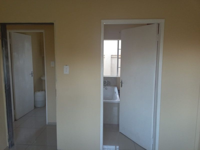 A neutral-toned hallway providing access to adjacent rooms, including a bathroom with a visible bathtub.