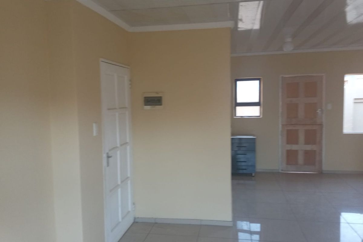 An empty, neutrally painted living area featuring tiled flooring, panelled doors, and a tiled ceiling, offering a blank canvas for interior design.