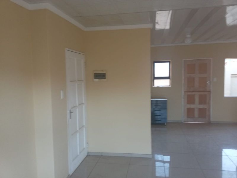 An empty, neutrally painted living area featuring tiled flooring, panelled doors, and a tiled ceiling, offering a blank canvas for interior design.