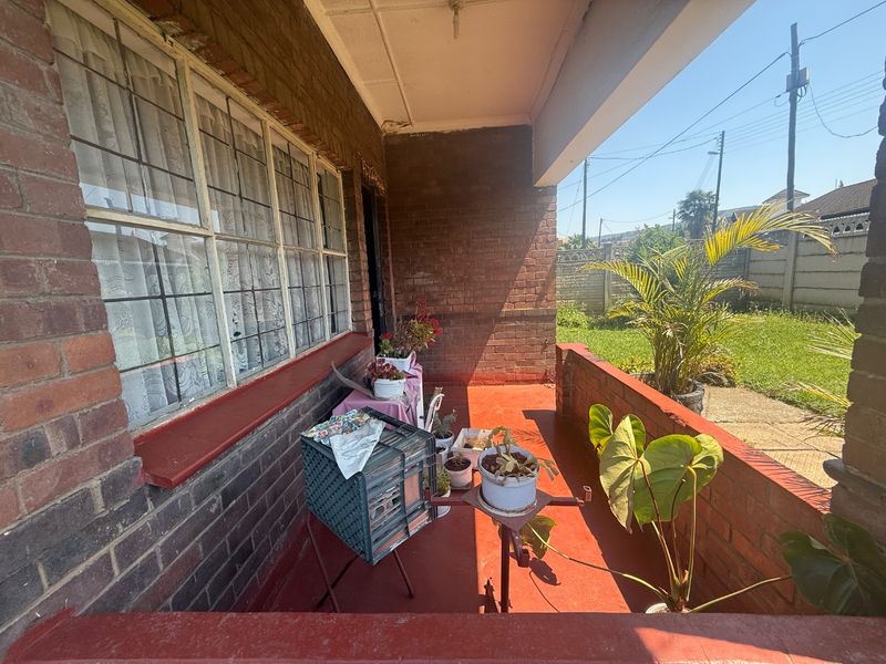 A covered brick patio area featuring a concrete floor and steel-framed windows, offering a functional outdoor space with potential for cosmetic updates.