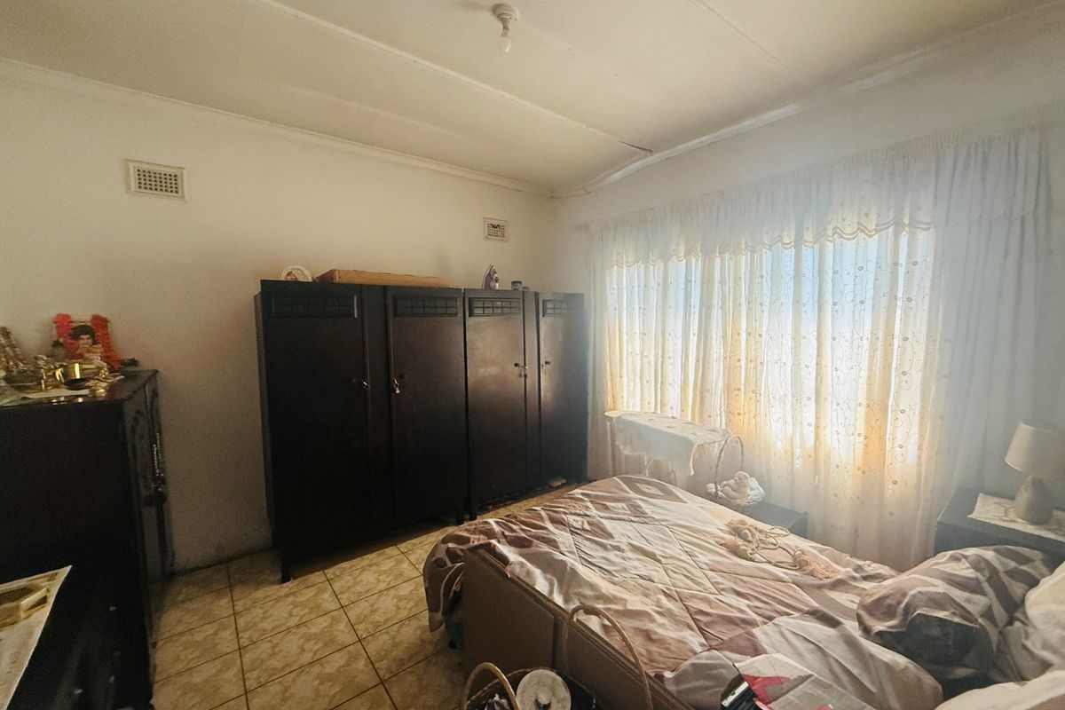 A bedroom featuring tiled flooring and natural light through window curtains, requiring some cosmetic updates to the ceiling and finishes.