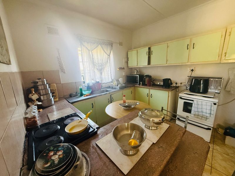 A functional kitchen featuring dated cabinetry, laminate countertops, a tiled splashback, and a freestanding electric oven with a hob.