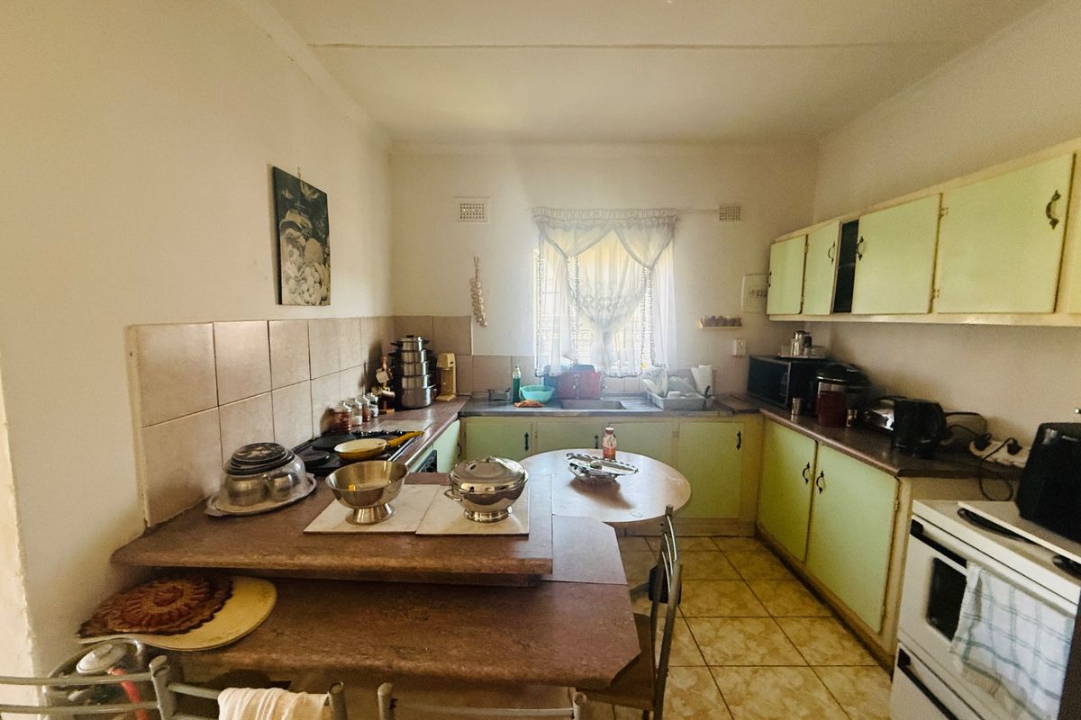 A functional kitchen featuring dated cabinetry, laminate countertops, tiled backsplash, and ceramic floor tiles, offering potential for a modern renovation.