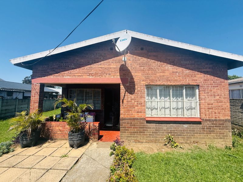 Front elevation of a single-story face brick house featuring a covered entrance porch, metal window frames, and a paved walkway.