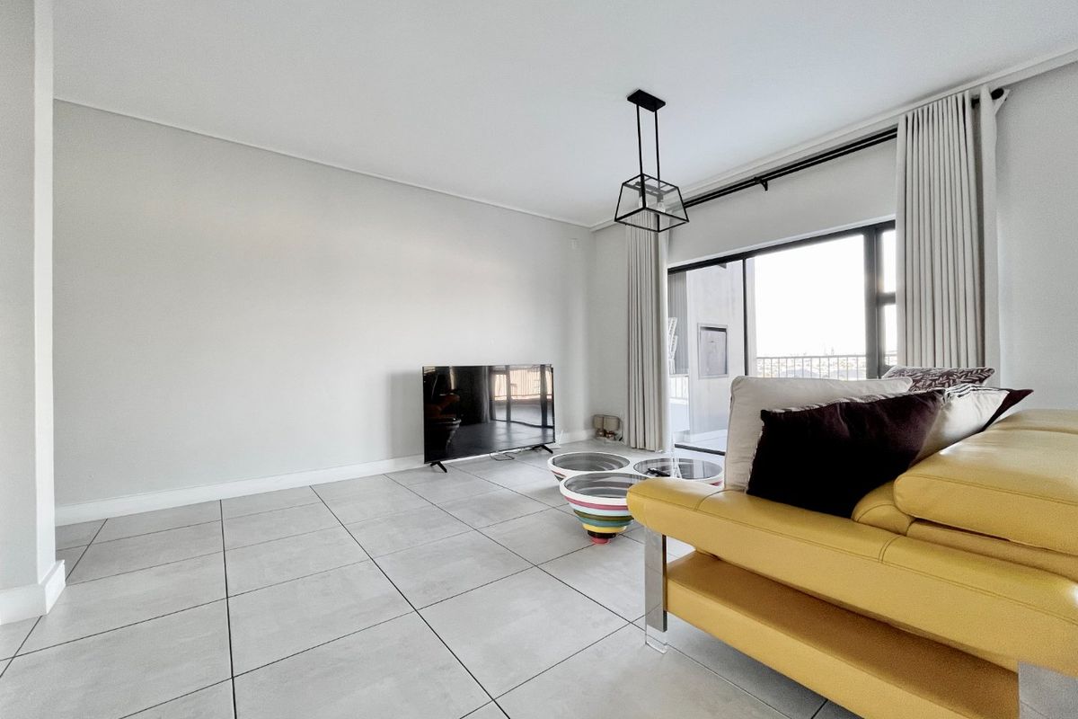 A bright and spacious living room featuring large format floor tiles, a modern pendant light, and a sliding glass door leading to a balcony.