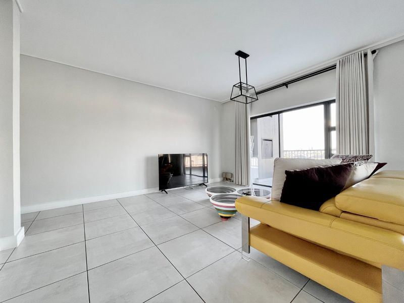 A bright and spacious living room featuring large format floor tiles, a modern pendant light, and a sliding glass door leading to a balcony.