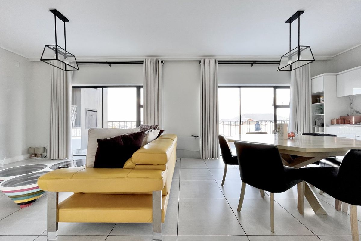 A bright open-plan living and dining area featuring large sliding glass doors, modern pendant lighting, and sleek tiled flooring throughout.