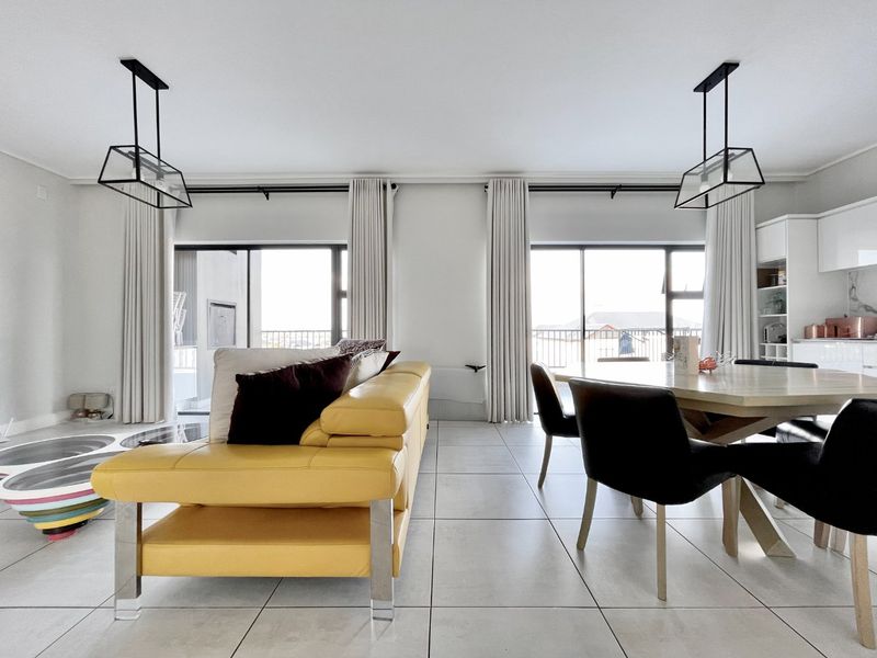 A bright open-plan living and dining area featuring large sliding glass doors, modern pendant lighting, and sleek tiled flooring throughout.