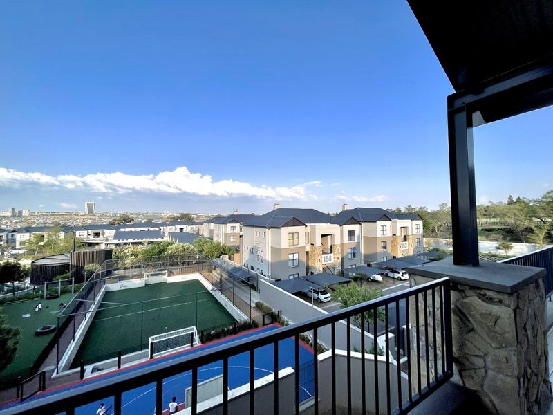 Elevated view from a balcony overlooking a residential complex with sports facilities, including a soccer field and basketball court.