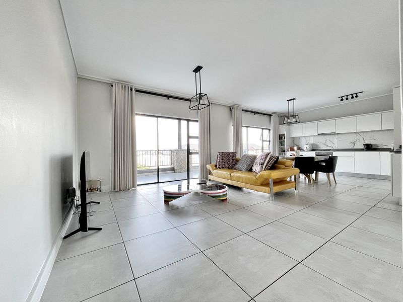 Spacious open-plan living and kitchen area featuring large format floor tiles, modern cabinetry, and seamless access to a private balcony.