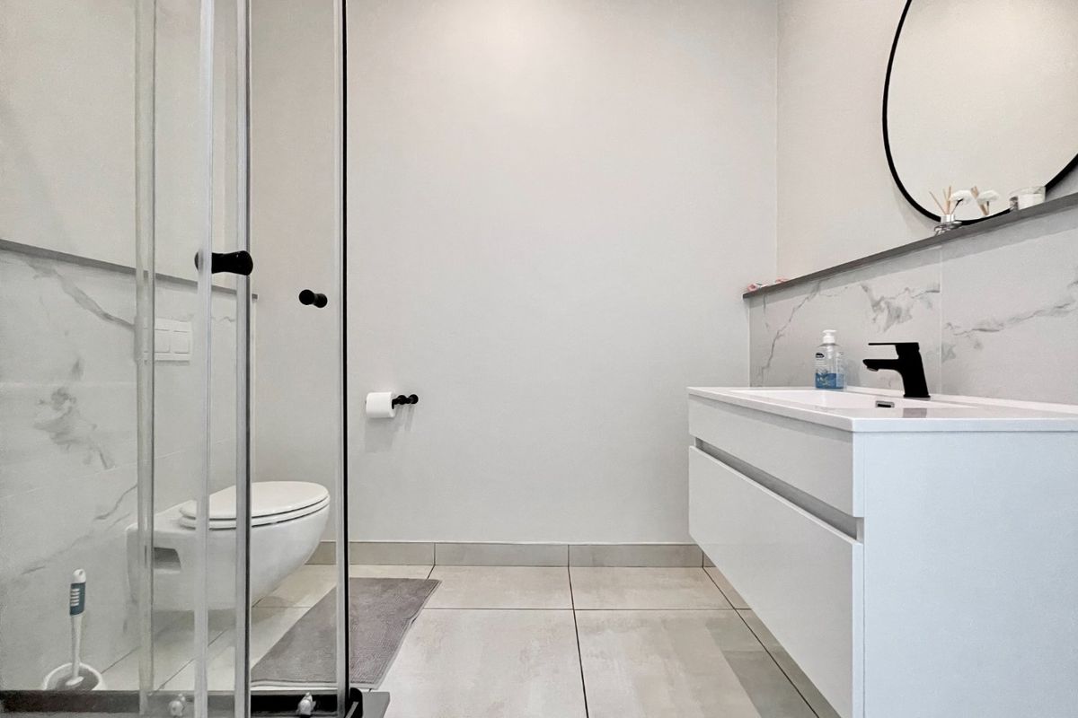 Modern bathroom featuring a wall-hung vanity, wall-hung toilet, glass shower enclosure, and elegant marble-look wall tiling with contemporary black fixtures.