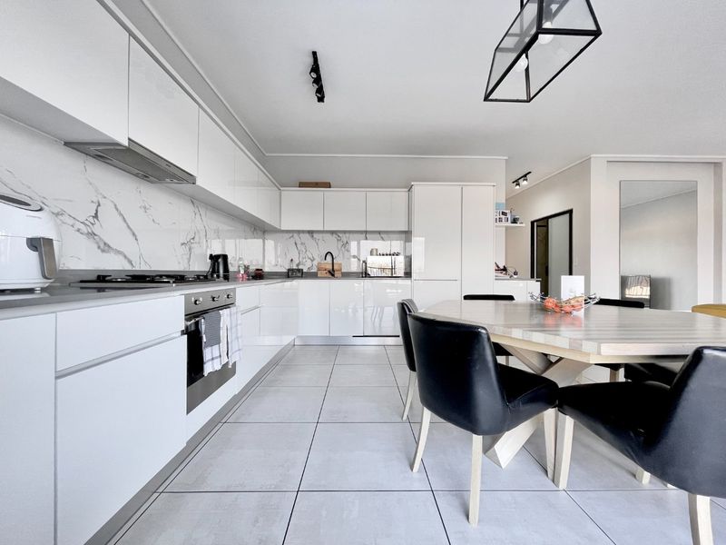 Modern open-plan kitchen featuring high-gloss white cabinetry, marble-look splashbacks, integrated appliances, and large format floor tiles, seamlessly flowing into the dining area.