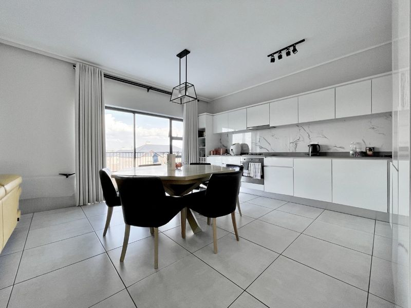 Modern open-plan kitchen and dining area featuring sleek white cabinetry, marble-look splashback, tiled floors, and direct access to a balcony through sliding glass doors.