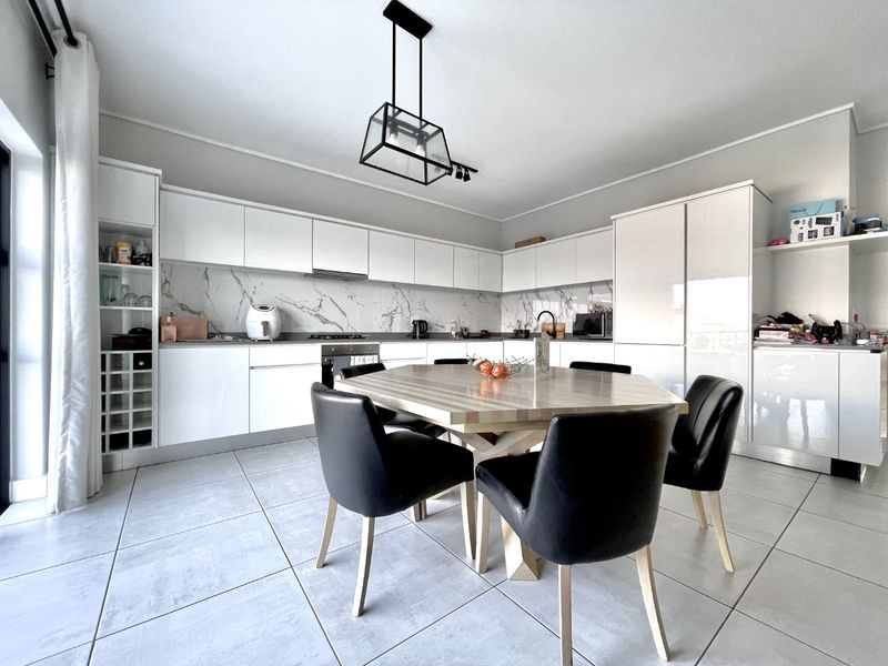Modern open-plan kitchen featuring white gloss cabinetry, marble-look splashback, integrated appliances, and tiled flooring, seamlessly flowing into the dining area.