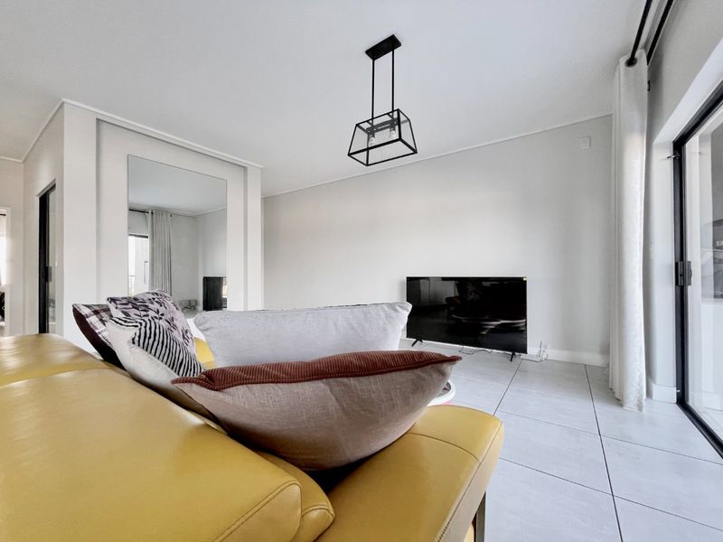 A bright and modern living room featuring large format floor tiles, a contemporary pendant light, and a sliding glass door leading to an outdoor area.