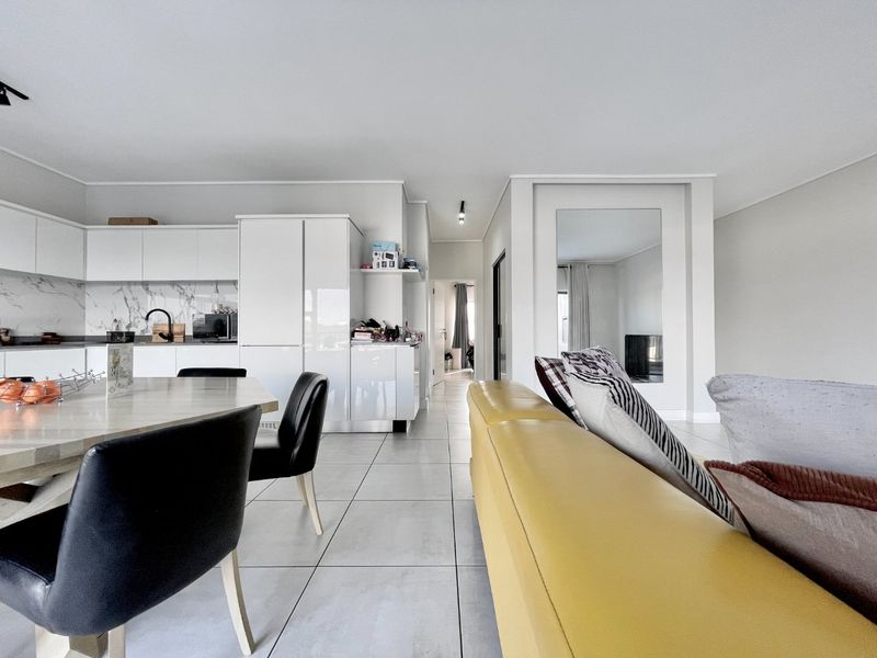 Modern open-plan living and kitchen area featuring white gloss cabinetry, marble-look splashback, and large format floor tiles in a bright, contemporary space.