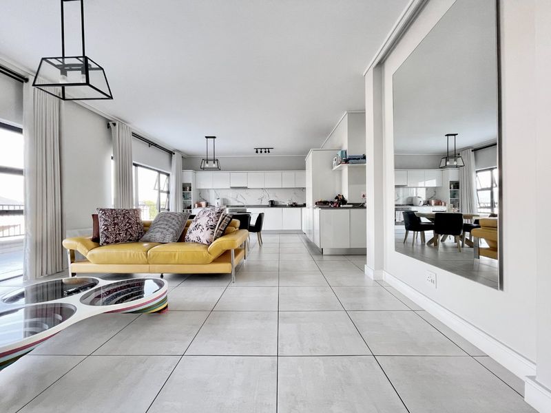 A bright and modern open-plan living and kitchen area featuring large format floor tiles, sleek white cabinetry, and a spacious, contemporary layout.