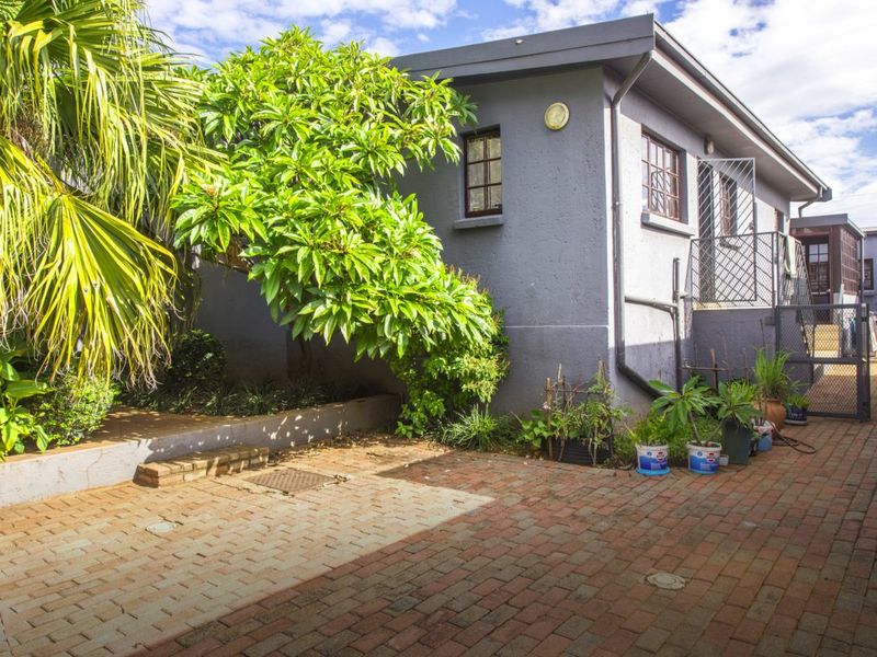 A view of the rear exterior area featuring brick paving, a retaining wall, and a secure side entrance to the property.